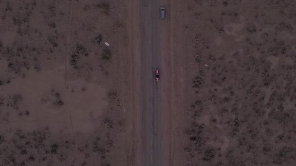 AERIAL: Birds View let přes opuštěnou opuštěnou pouštní silnici s červeným autem v dálce — Stock video