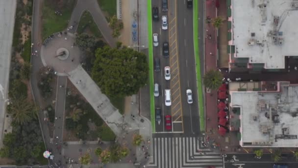 AERIAL: Vista de Birdseye del muelle de Santa Mónica, la intersección de Los Ángeles y la autopista de la costa del Pacífico PCH con peatones ligeros, tráfico de automóviles y aves que pasan al atardecer — Vídeo de stock