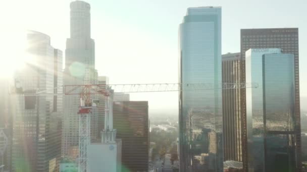 AERIAL: Közel az építési telek felhőkarcoló daru Los Angeles belvárosában, Kalifornia Skyline gyönyörű kék ég és napos hangulatú nap — Stock videók