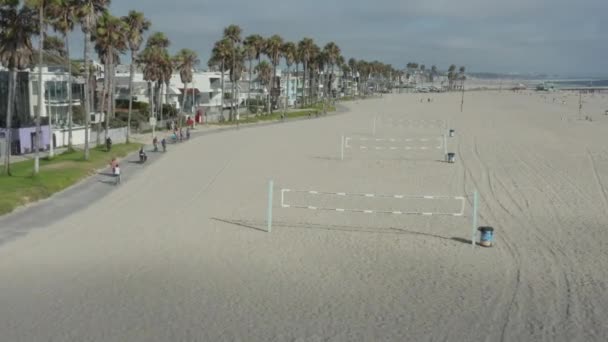 AERIAL: 야자나무와 자전거 전용 도로, 로스앤젤레스 Sunny, Venice Beach 에서 배구 그물을 가지고 해변을 비행하는 모습 — 비디오