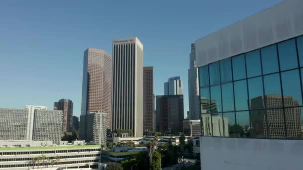 AERIAL: Onthulling van Downtown Los Angeles, California Skyline achter gebouw met glazen ramen op mooie blauwe hemel en zonnige dag — Stockvideo