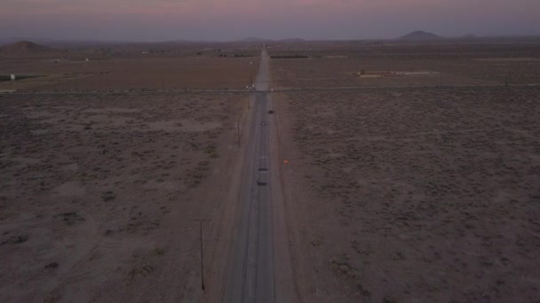 AERIAL: Vuelo sobre la solitaria carretera desierta abandonada con coche rojo conduciendo en la distancia — Vídeo de stock