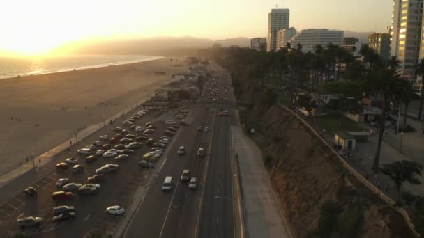 AERIAL: Utsikt över Pacific Coast Highway PCH bredvid Santa Monica Pier, Los Angeles med lätt trafik och havsutsikt vid solnedgången vågor, sommar — Stockvideo