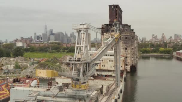 AERIAL: Sobre la vieja grúa oxidada de carga y el almacén con el horizonte de la ciudad de Nueva York en segundo plano en un día nublado gris — Vídeos de Stock