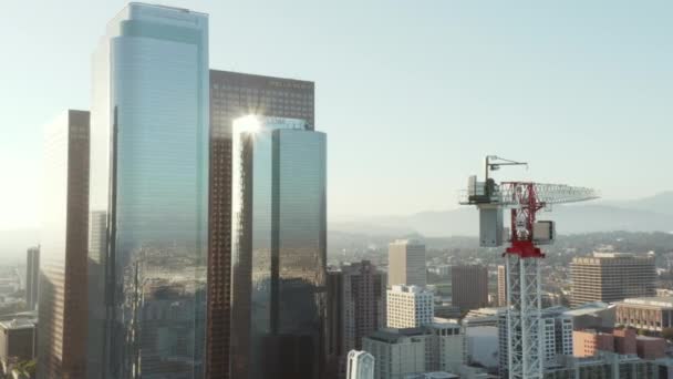 AERIAL: Közel az építési telek felhőkarcoló daru Los Angeles belvárosában, Kalifornia Skyline gyönyörű kék ég és napos hangulatú nap — Stock videók