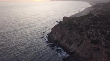 Malibu, California 'da sahil şeridi manzaralı Paficic Okyanusu üzerinde gün batımında dağ yamacıyla uçmak