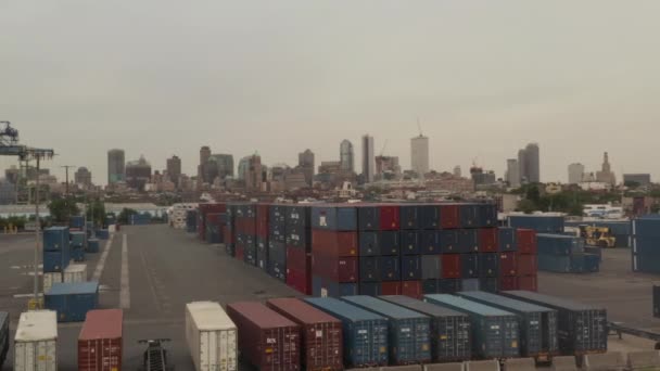 AERIAL: Piros és kék ipari teherkonténerek felett repül a kikötőben New York City-vel, háttérben a felhős napon — Stock videók