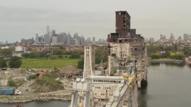 AÉRIAL : Sur une vieille grue et un entrepôt rouillés avec New York City Skyline en arrière-plan par une journée nuageuse grise — Video