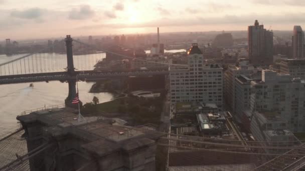 AERIAL: Närbild av Brooklyn Bridge med amerikansk flagga och vacker soluppgång morgon ljus över östra floden New York City — Stockvideo