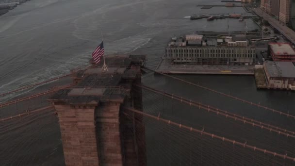 AERIAL: Vuelo en círculo sobre el puente de Brooklyn con bandera americana y vista al East River Manhattan New York City Skyline — Vídeos de Stock