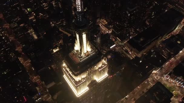 AERIAL: lélegzetelállító kör felett ikonikus Empire State Building felett világított párhuzamos utak és csomópontok lakóházak és irodaházak Midtown Manhattan, New York City éjjel — Stock videók