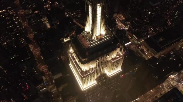 AERIAL: Impresionante círculo sobre el icónico Empire State Building arriba iluminado avenidas paralelas y uniones condominios residenciales y edificios de oficinas en Midtown Manhattan, Nueva York por la noche — Vídeos de Stock