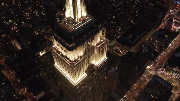 AERIAL: Dech beroucí let nad ikonickou Empire State Building nahoře osvětlil paralelní cesty a křižovatky obytných bytů a kancelářských budov v Midtown Manhattan, New York City v noci — Stock video