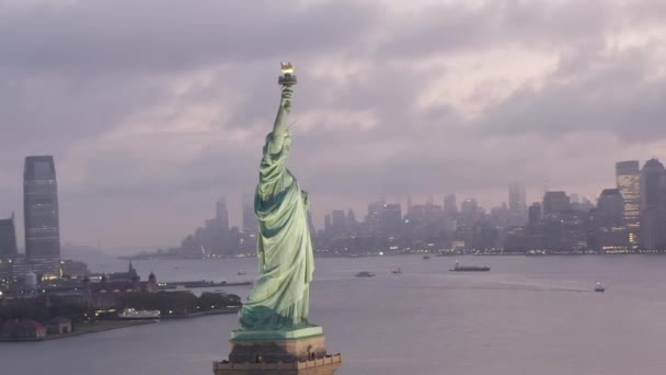 AERIAL: Circling Statuia Libertății iluminat în lumina dimineții devreme cu ceață New York City Skyline în fundal — Videoclip de stoc