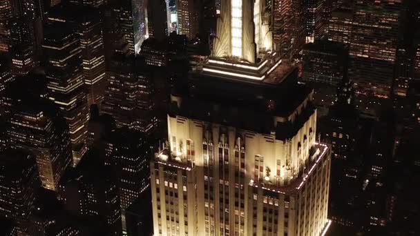 AERIAL:象徴的なエンパイアステートビルの上の息をのむようなサークルは、夜にニューヨーク州マンハッタンのミッドタウンにある平行な道とジャンクションの住宅マンションやオフィスビルを照らし出しました。 — ストック動画