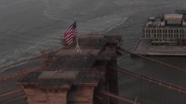 AERIAL: Close up circle flight over Brooklyn Bridge with American flag and East River view Manhattan New York City Skyline — 图库视频影像