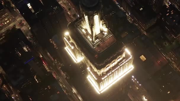 AERIAL: Häpnadsväckande flygning över den ikoniska Empire State Building ovan lyste upp parallella avenyer och korsningar bostäder och kontorsbyggnader i Midtown Manhattan, New York City på natten — Stockvideo