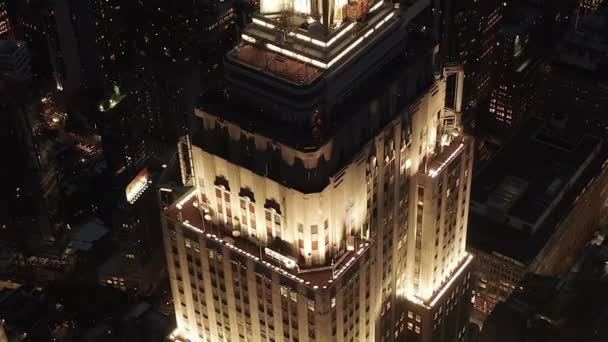 AERIAL: Impresionante vuelo sobre el icónico Empire State Building iluminó avenidas paralelas y uniones condominios residenciales y edificios de oficinas en Midtown Manhattan, Nueva York por la noche — Vídeos de Stock