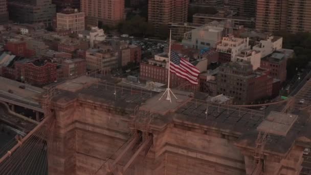 AERIAL: Close up voo círculo sobre Brooklyn Bridge com bandeira americana e East River vista Manhattan New York City Skyline — Vídeo de Stock