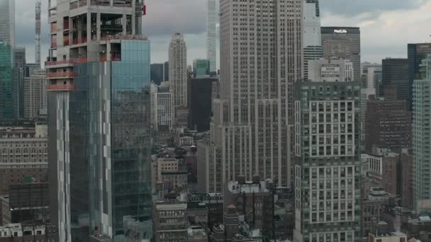 空気:曇りの日に忙しい街のスクラッパーに囲まれたマンハッタンのエンパイアステートビルを飛ぶ — ストック動画