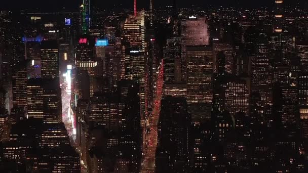 AERIAL：令人叹为观止的是，位于纽约市曼哈顿中城的标志性帝国大厦在夜间点亮了平行的街道和交叉口、住宅公寓和办公大楼 — 图库视频影像