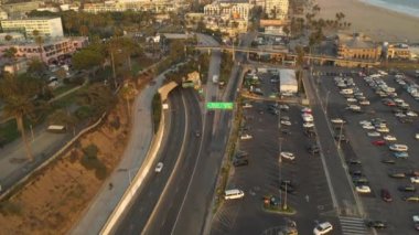 Santa Monica İskelesi, Los Angeles otoparkı üzerinde, gün batımında geçen kuşların ve trafik ışıklarının kesiştiği kıyıya doğru. 