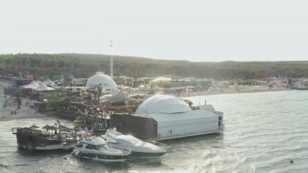 AERIAL: Vacker strandklubb i Novalia, Kroatien vid havet med Yachts i soligt väder och flaggor, Palmer och Blå vattenvågor — Stockvideo