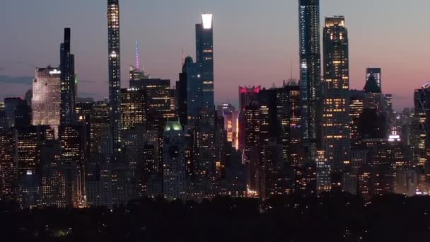 AERIAL: Amplia vista del horizonte de Manhattan por la noche con luces parpadeantes de la ciudad y nuevos rascacielos en la ciudad de Nueva York en Central Park — Vídeos de Stock