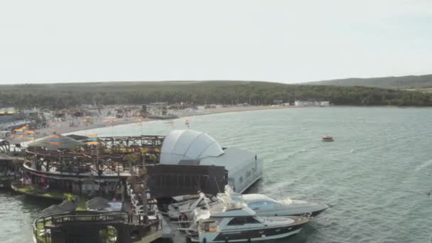 AERIELL: Vacker strandklubb i Novalia, Kroatien vid havet med Yachts i soligt väder och flaggor, Palmer och Blå vattenvågor — Stockvideo