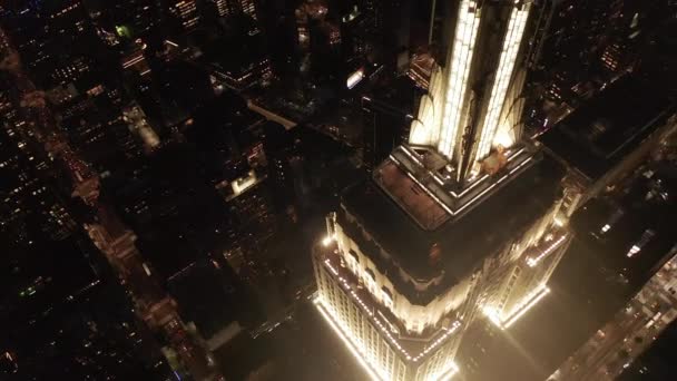 AERIAL: Adembenemende cirkel over het iconische Empire State Building boven verlichtte parallelle wegen en knooppunten residentiële flatgebouwen en kantoorgebouwen in Midtown Manhattan, New York City 's nachts — Stockvideo