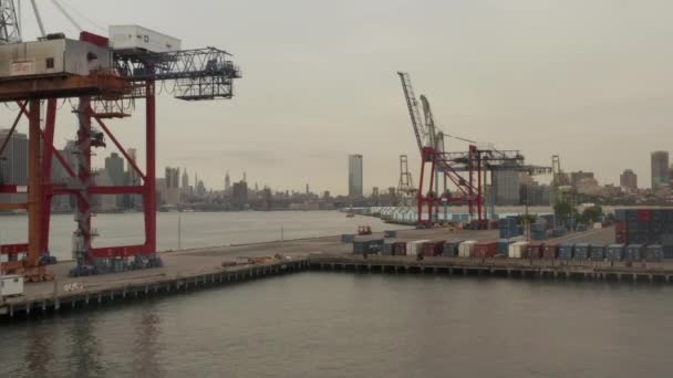 AERIAL: Vliegende rondvliegende industriële kranen in dokken met New York City skyline op achtergrond en rivier — Stockvideo