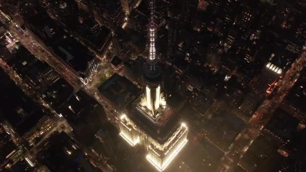 AÉRIAL : Vol à couper le souffle au-dessus de l'emblématique Empire State Building au-dessus éclairé avenues parallèles et jonctions condominiums résidentiels et immeubles de bureaux dans Midtown Manhattan, New York City la nuit — Video