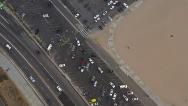 AERIAL: Olhando para cima sobre estacionamento revelando Santa Monica Pier, Los Angeles de cima na bela Sunset with Tourists, Pedestres se divertindo na Ferrys Wheel com ondas vista mar bater — Vídeo de Stock