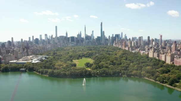 АЭРИАЛ: вид на Центральный парк с озером и Манхэттенским небоскребом на фоне солнечного летнего дня в Нью-Йорке — стоковое видео