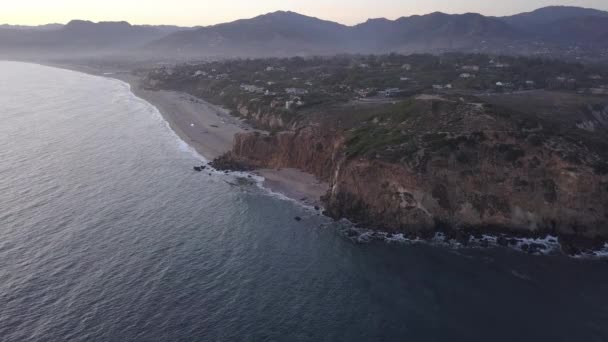 AERIAL: voo sobre Malibu, Califórnia vista da praia Shore Line Oceano Paficic ao pôr do sol com penhasco de montanha — Vídeo de Stock