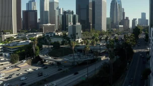 AERIAL: Hacia el centro de Los Ángeles, California tráfico de intersección con palmeras y Skyline en el fondo en el hermoso cielo azul y día soleado — Vídeo de stock