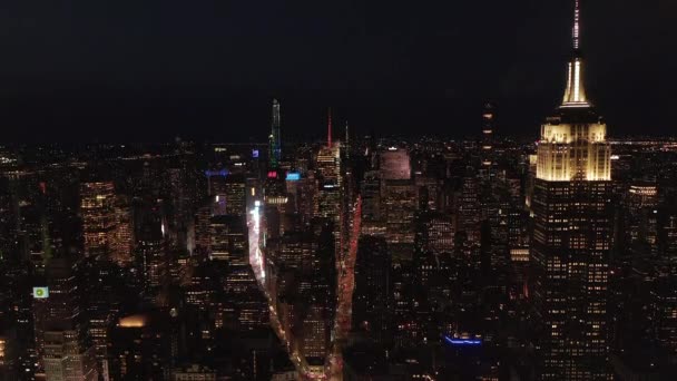 AERIAL: Adembenemend weids uitzicht op het iconische Empire State Building boven verlichtte parallelle wegen en knooppunten residentiële flatgebouwen en kantoorgebouwen in Midtown Manhattan, New York City 's nachts — Stockvideo