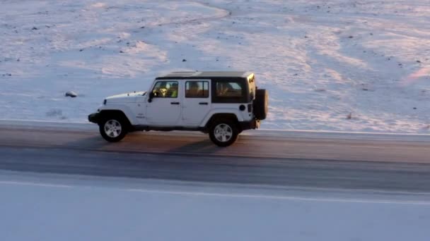 AERIAL: Cierre tras el jeep de lado por la carretera de nieve en Islandia en Sunset Winter, Sun, Arctic. — Vídeos de Stock