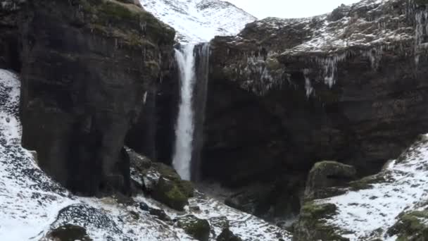 AERIAL: Vliegen richting waterval in de sneeuw, IJskloof in IJsland Green Grass, bewolkt — Stockvideo