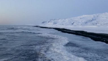 İzlanda 'da kar, buz, dalga, su gibi arka planda beyaz arktik kar dağlarıyla Kara Kumsal üzerinde uçmak