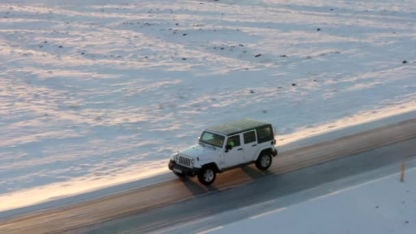 AERIAL: Repülés mellett Jeep havas úton Izlandon naplementekor tél, nap, sarkvidék — Stock videók