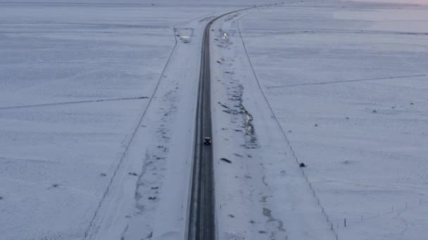 AERIAL:アイスランドの冬、日没、北極の車に続く道路と雪の白い風景 — ストック動画