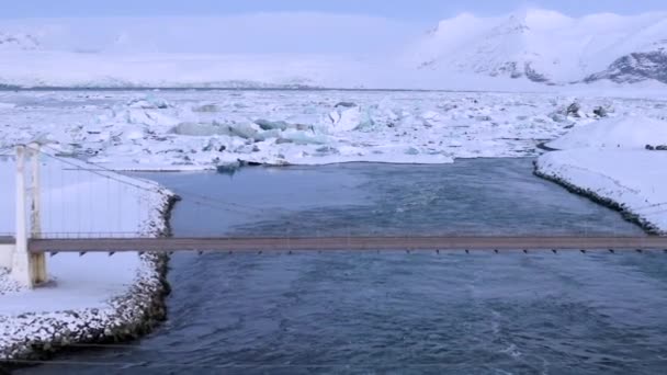 AERIAL: Volando sobre el puente con coche que conduce hacia los témpanos de hielo nevados en Islandia Lago Invierno, Nieve — Vídeos de Stock