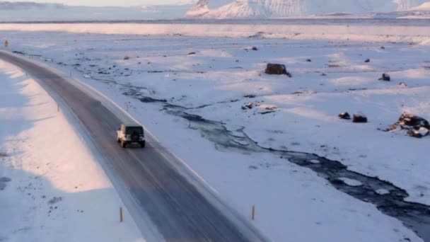AERIAL: Paisagem Branca de Neve com Estrada seguindo Jeep na Islândia ao pôr do sol Inverno, Sol, Árctico — Vídeo de Stock