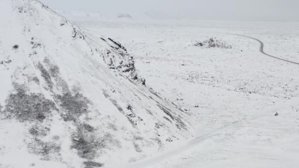 AERIAL: 아이슬란드 겨울에 검은 바위가 있는 백설 산에 눈이 내리는 추운 북극 — 비디오