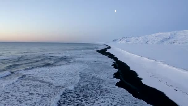 AERIAL: Repülő felett Black Beach fehér sarkvidéki hegyek háttérben Izlandon téli hó, Jég, Hullámok, Víz — Stock videók