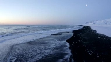 İzlanda 'da kar, buz, dalga, su gibi arka planda beyaz arktik kar dağlarıyla Kara Kumsal üzerinde uçmak
