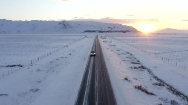 AERIAL: Primer plano de la conducción en jeep en Islandia carretera con montañas blancas como la nieve y la puesta del sol Nieve, Ártico — Vídeos de Stock