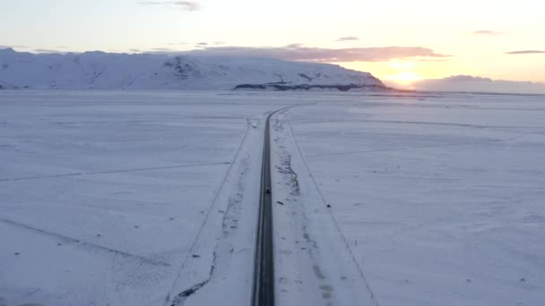 AERIAL: Paisagem branca de neve com estrada seguindo carro na Islândia Inverno, pôr do sol, Ártico — Vídeo de Stock