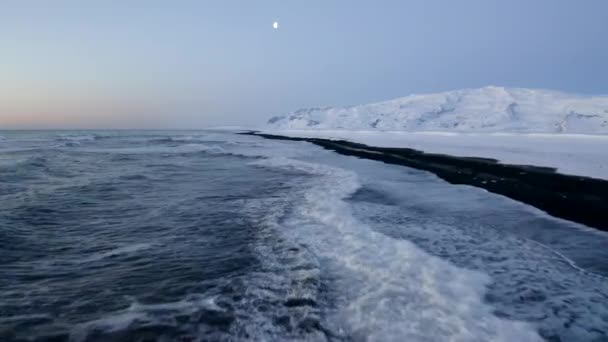 AERIAL: Voando sobre Black Beach com montanhas brancas de neve ártica no fundo na Islândia no inverno Neve, Gelo, Ondas, Água — Vídeo de Stock